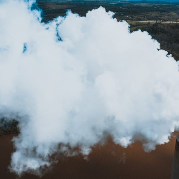 vapor from stone tower above woods and river in factory