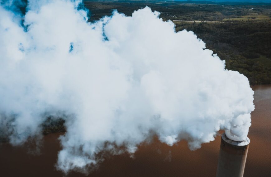vapor from stone tower above woods and river in factory