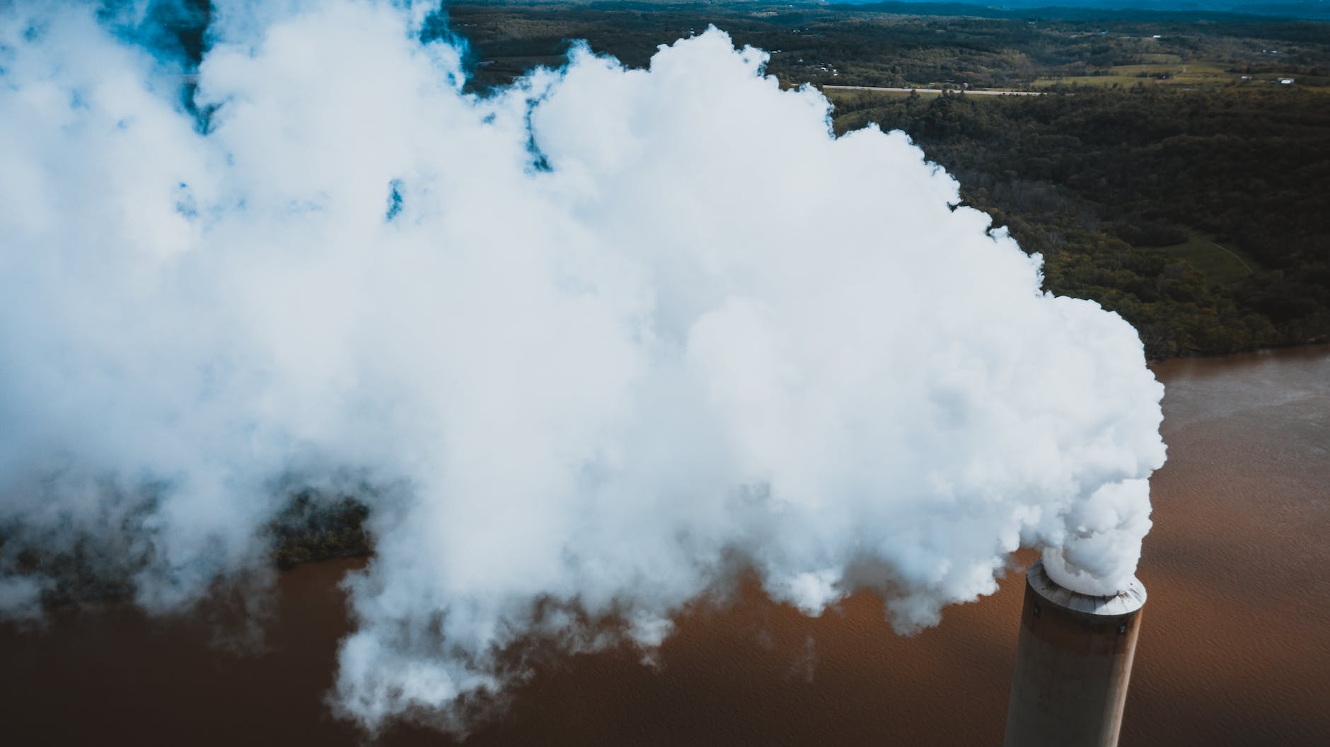 vapor from stone tower above woods and river in factory